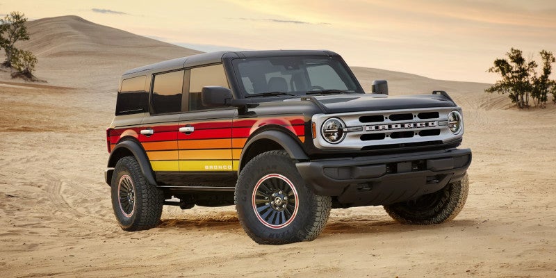 Black 4-door Ford Bronco with retro red, orange, and yellow stripes on the side, parked in a desert landscape.