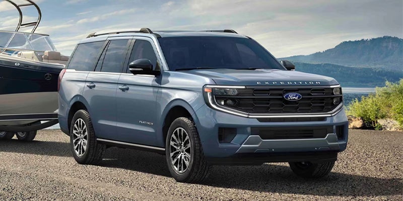 A blue Ford Expedition SUV towing a boat on a gravel road