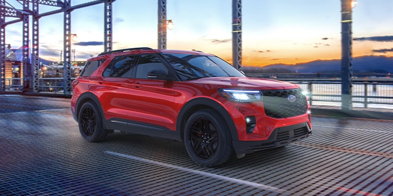 A red Ford Explorer SUV parked on a metal grate bridge at sunset