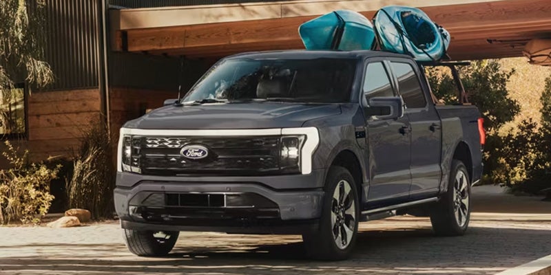 A dark grey Ford F-150 pickup truck with two blue kayaks on the roof rack.